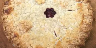 A whole baked pie with a crimped crust and a central vent hole, resting on a wooden cutting board.