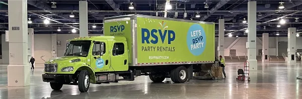 A green RSVP Party Rentals box truck parked inside a large warehouse with a worker loading equipment.