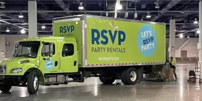 A green RSVP Party Rentals box truck parked inside a large warehouse with a worker loading equipment.