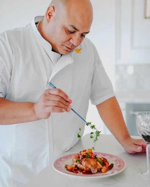 A chef in a white uniform carefully plating a meal with a garnish.