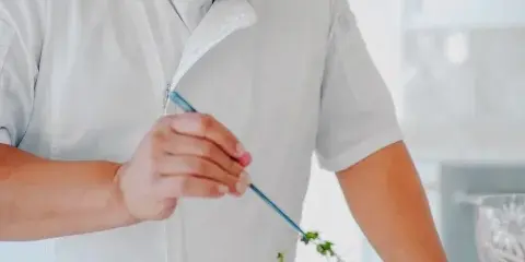 A chef in a white uniform carefully plating a meal with a garnish.