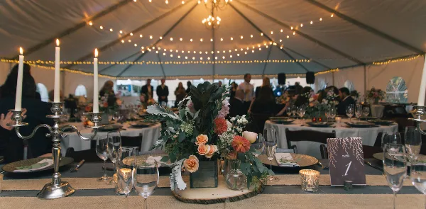 A decorated wedding table with floral centerpieces and candles set up inside a large white event tent.