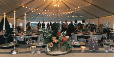 A decorated wedding table with floral centerpieces and candles set up inside a large white event tent.