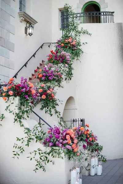A staircase decorated with cascading floral arrangements featuring orange and purple flowers and greenery.