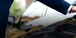 A professional chauffeur in a dark suit opening the door of a black luxury sedan.