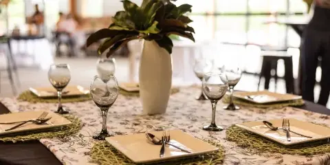 A set dining table with floral centerpiece and glassware inside a bright event venue with large glass doors.